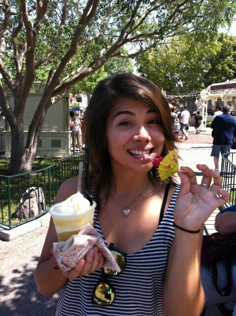 a woman eating an ice cream sundae in front of a tree with people walking around