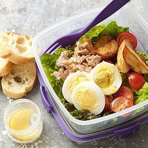 a plastic container filled with food next to bread and dressings on top of a table