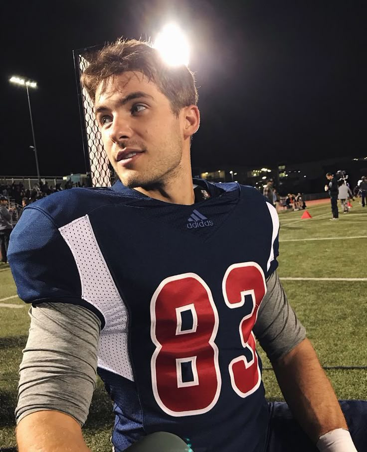 a man sitting on top of a field wearing a football uniform