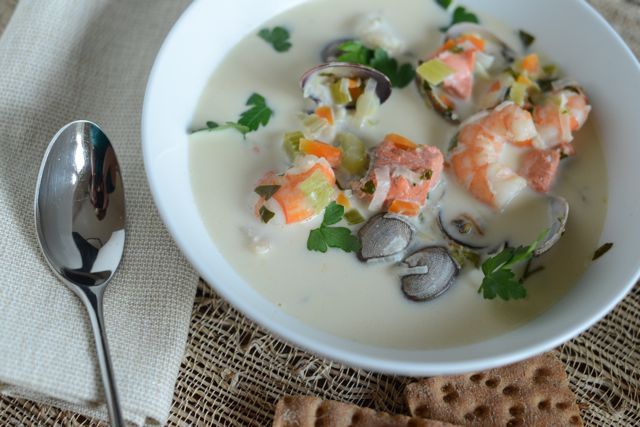 a bowl of soup with shrimp, clams and mushrooms on a table next to crackers