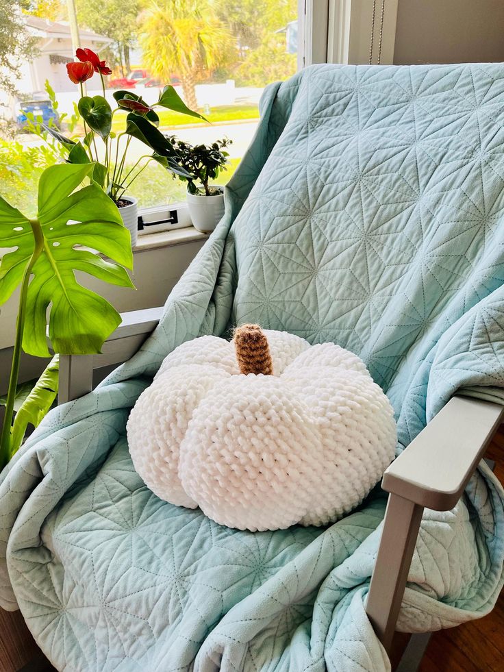 a white pumpkin shaped pillow sitting on top of a blue chair next to a window