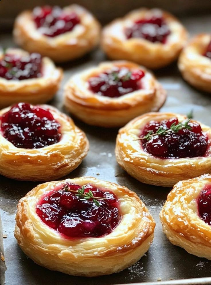 small pastries with jam on them sit in a baking pan, ready to be baked