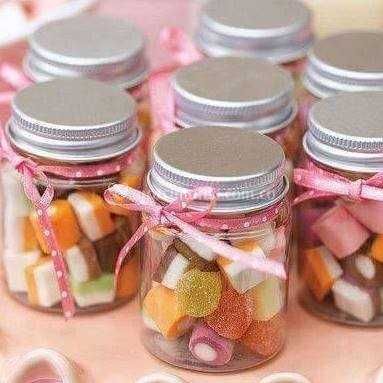 four glass jars filled with candy sitting on top of a pink tablecloth covered table