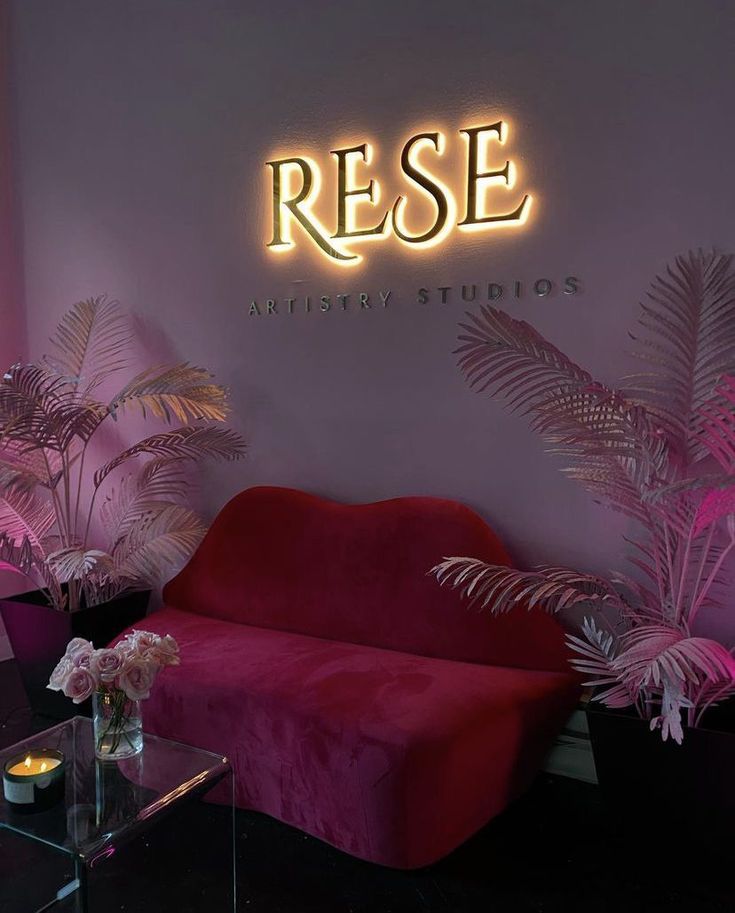 a pink couch sitting in front of a neon sign that reads rese artisan studios