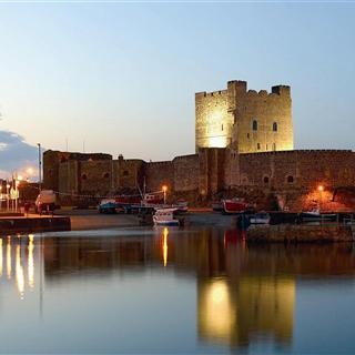 an old castle is lit up at night by the water's edge with boats in it