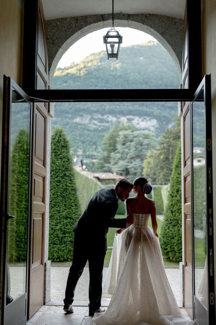 a bride and groom are standing in an open doorway with mountains in the back ground