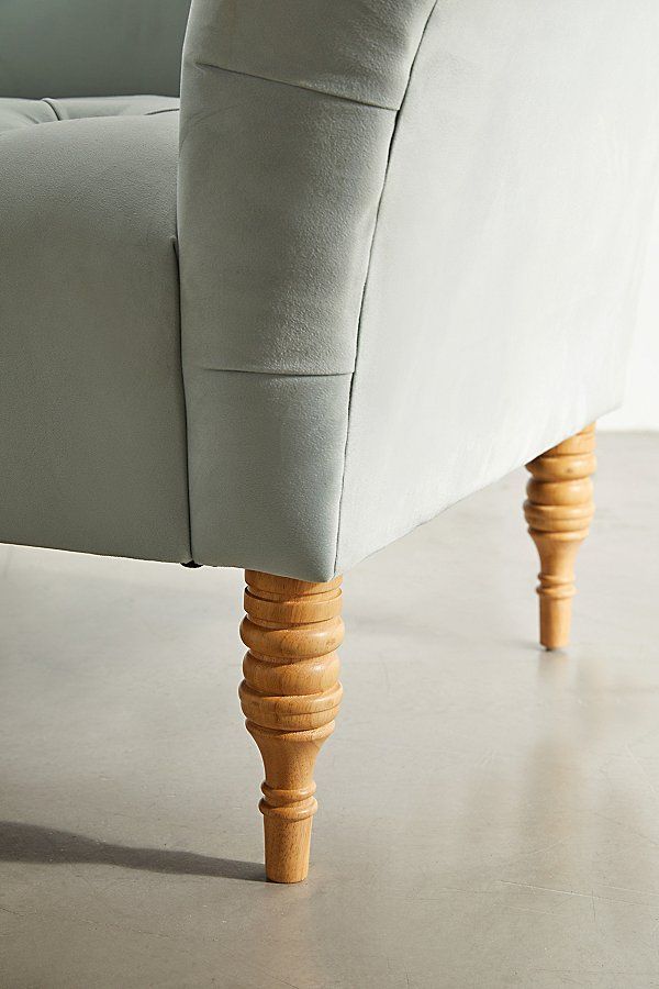 an upholstered couch with wooden legs and cushion on concrete floored room area