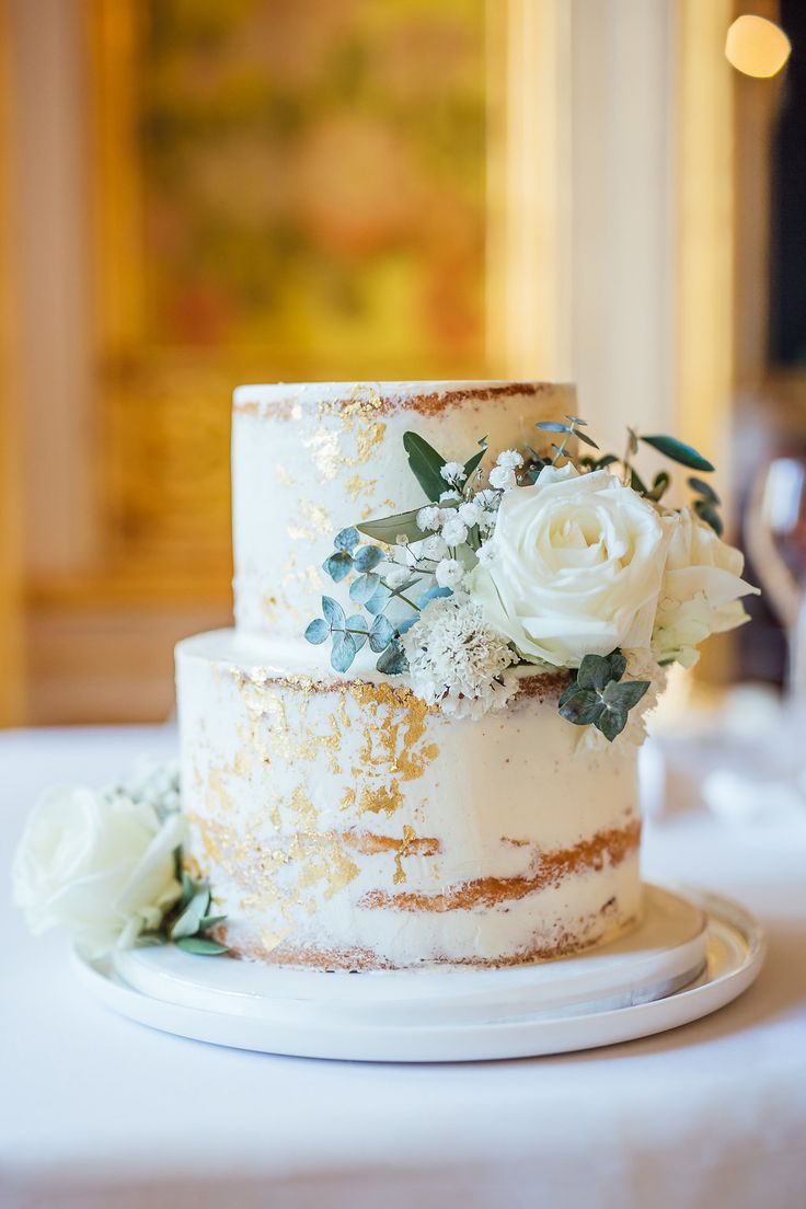 a three tiered cake with white flowers and greenery sits on a small plate