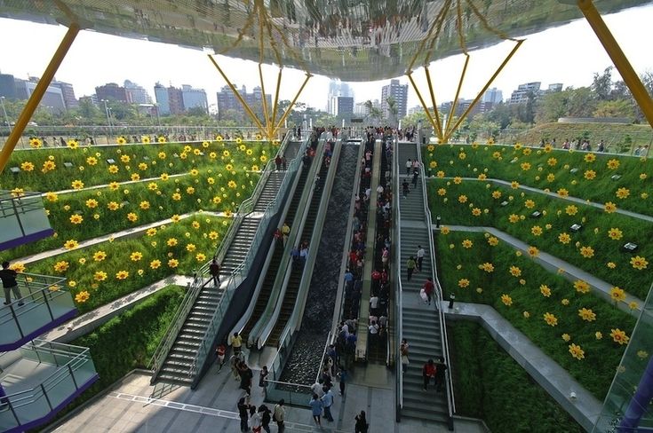 people are riding down an escalator with flowers growing on the walls and green roof