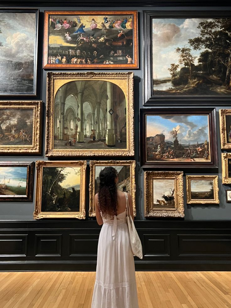 a woman in a white dress looking at paintings