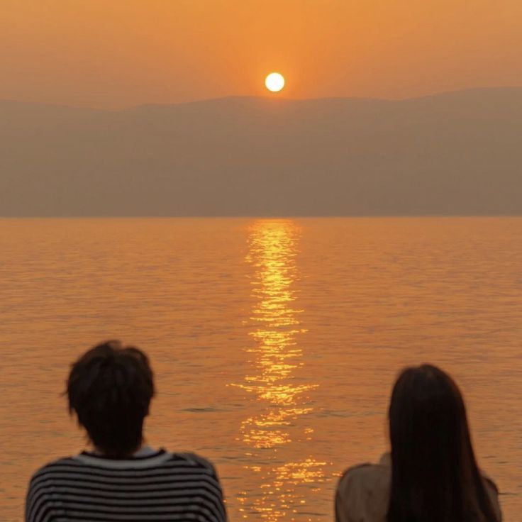 two people watching the sun set over water