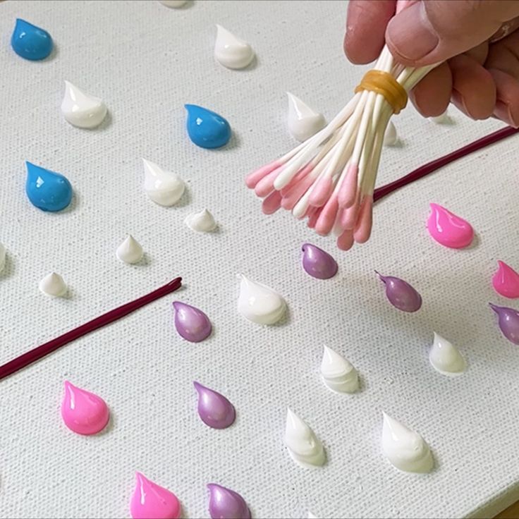 a person holding a whisk over some candy drops on a sheet of paper