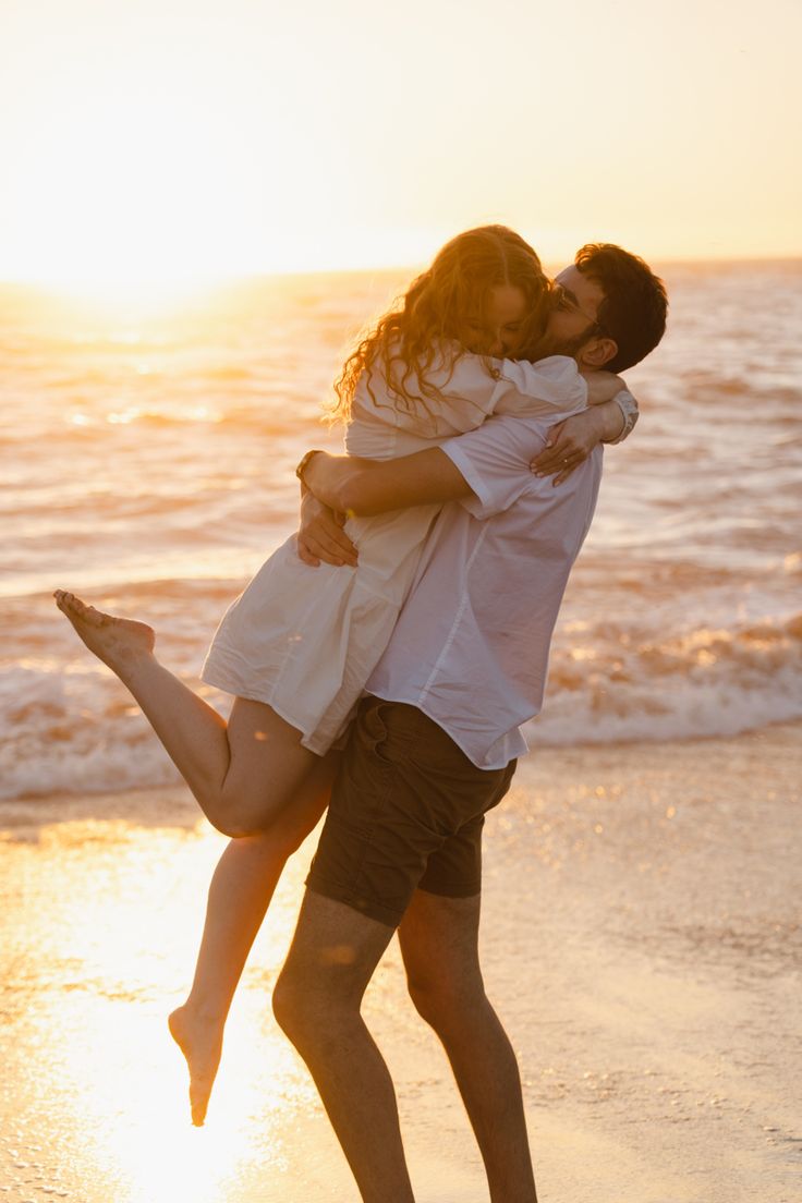 a man and woman hug on the beach as the sun sets