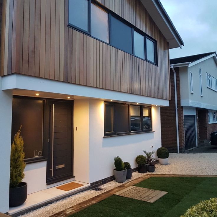 a modern house with wooden siding and black doors at dusk in front of the home