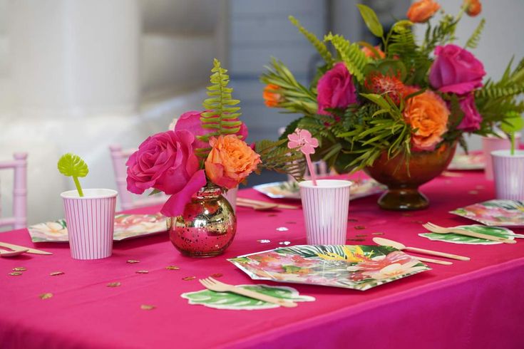 the table is set with pink and orange flowers in vases, plates and napkins