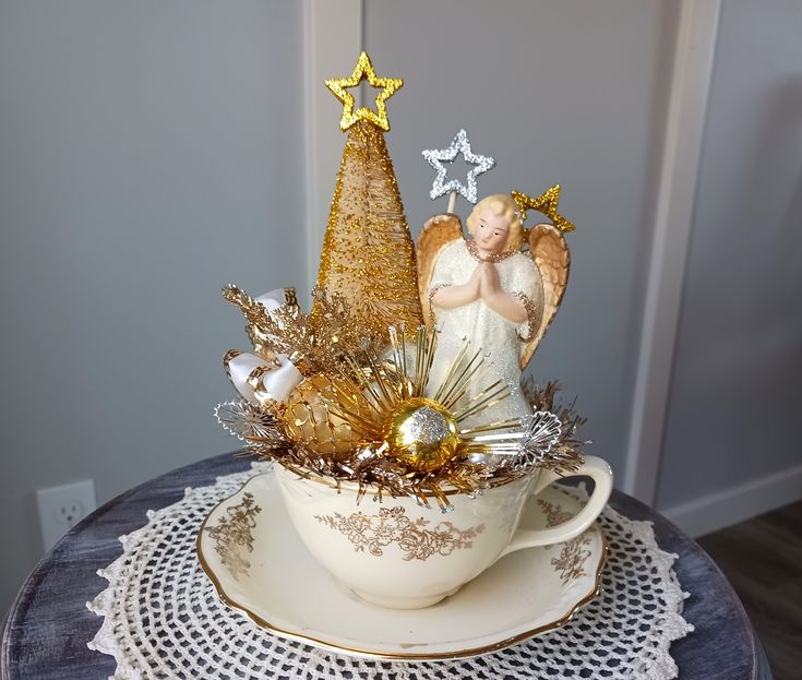 an angel figurine sitting on top of a teacup filled with christmas decorations