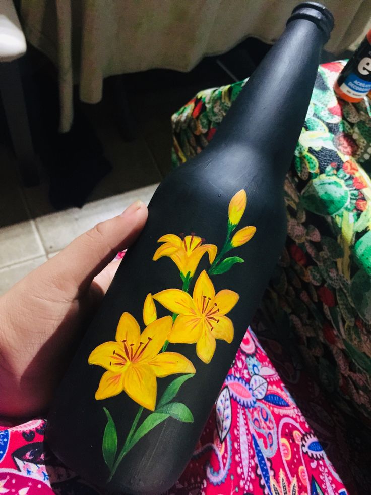 a hand holding a black bottle with yellow flowers painted on it