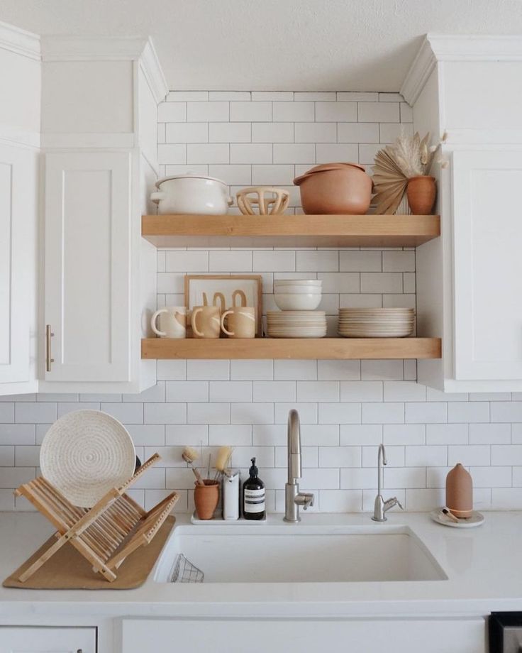 a kitchen with white cabinets and open shelving above the sink that is filled with dishes