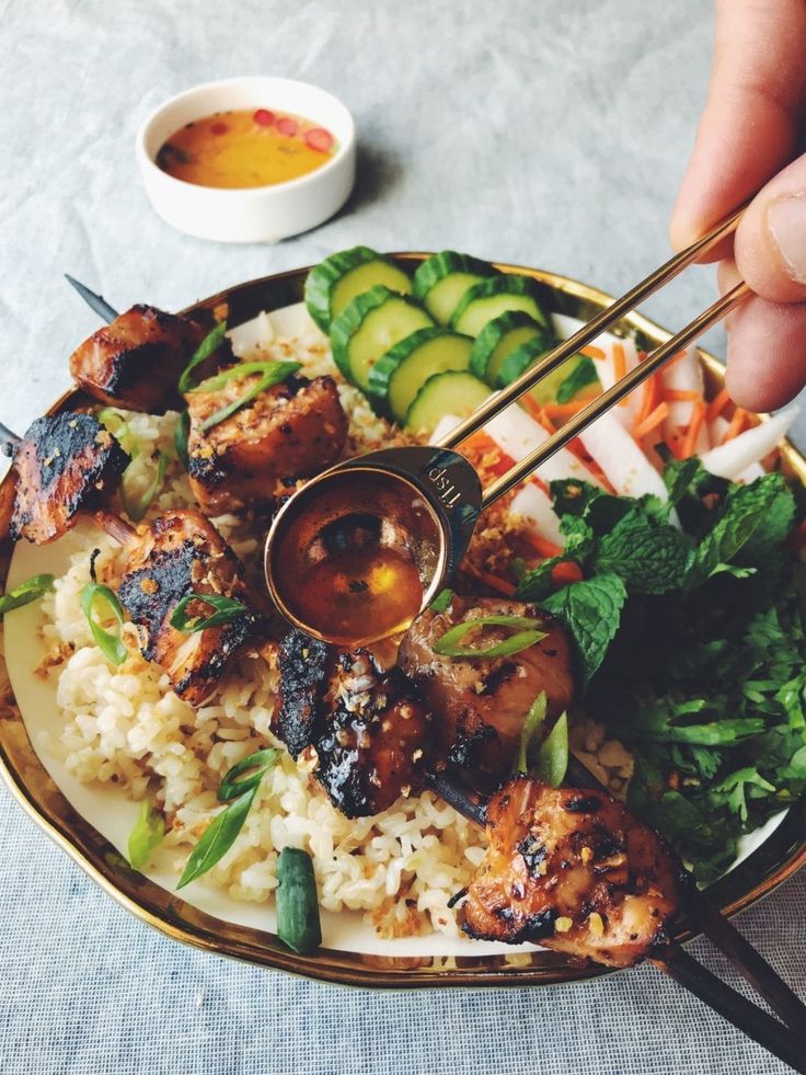 a person holding chopsticks over a plate of food with rice, cucumbers and sauce