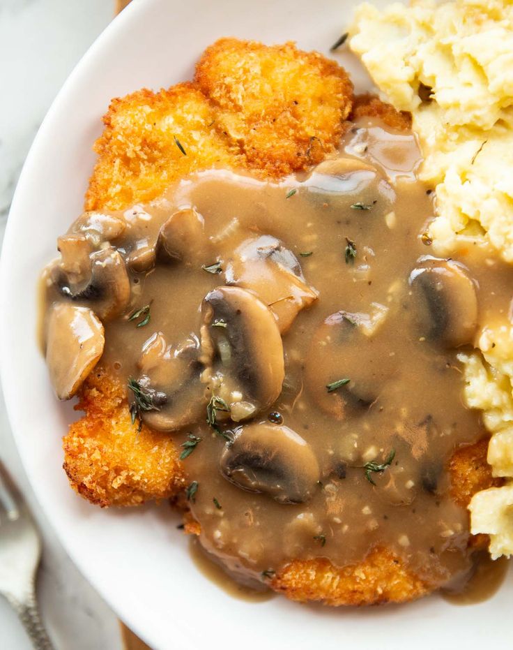 a white plate topped with meat covered in gravy next to mashed potatoes