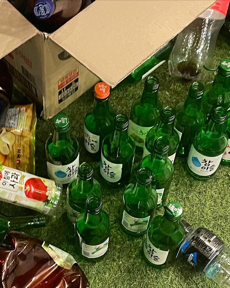 there are many green bottles on the ground next to each other and some drinks in plastic bags