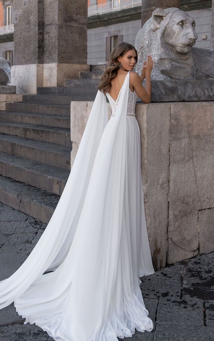 a woman in a white wedding dress standing next to a lion statue and stone steps