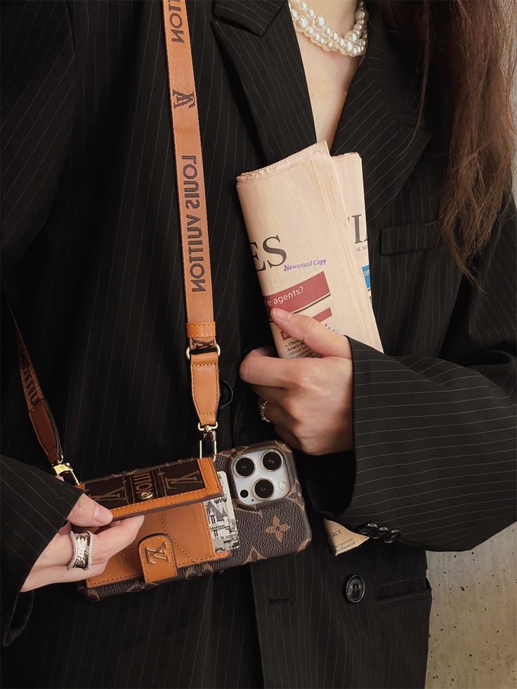 a woman in a business suit holding a cell phone case and purse with her name on it