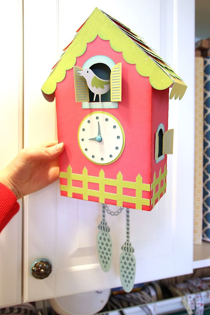 a hand is holding up a paper clock that looks like a bird on top of a house