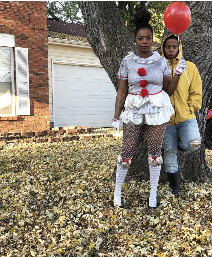 two people dressed up as clowns in front of a tree with balloons and leaves on the ground