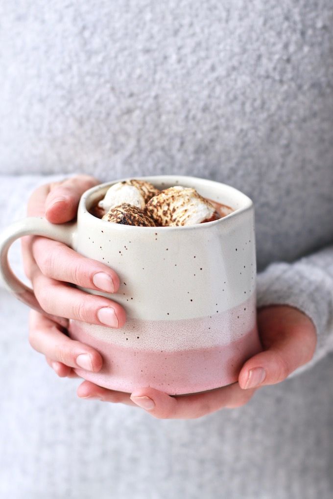 a woman is holding a cup with marshmallows in it and her hands