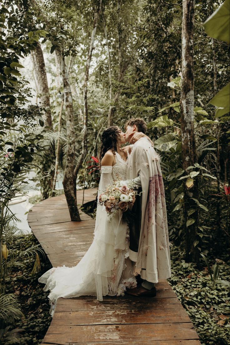 a bride and groom kissing on a wooden walkway in the forest with lush greenery