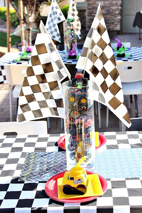 the table is decorated with checkered black and white tables cloths, yellow plastic toy cars in a glass vase