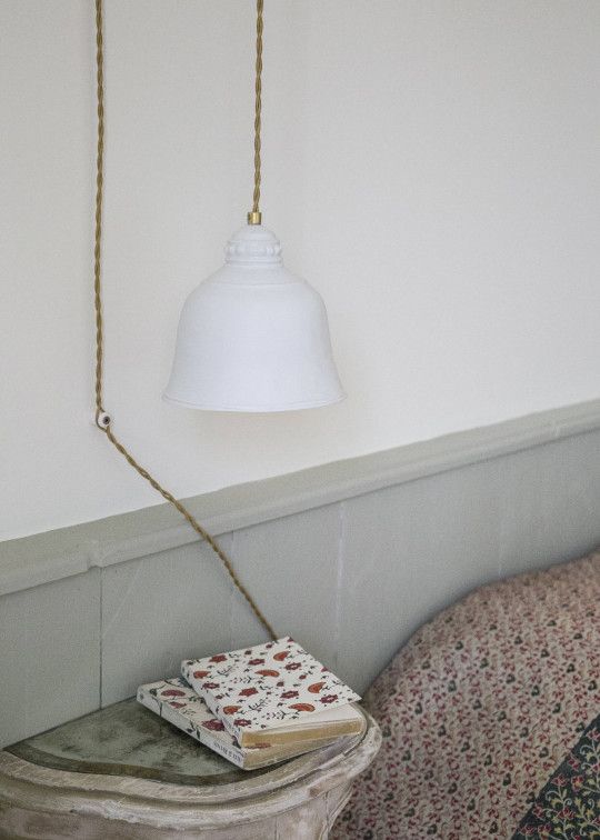 a white light hanging over a bed next to a book on top of a table