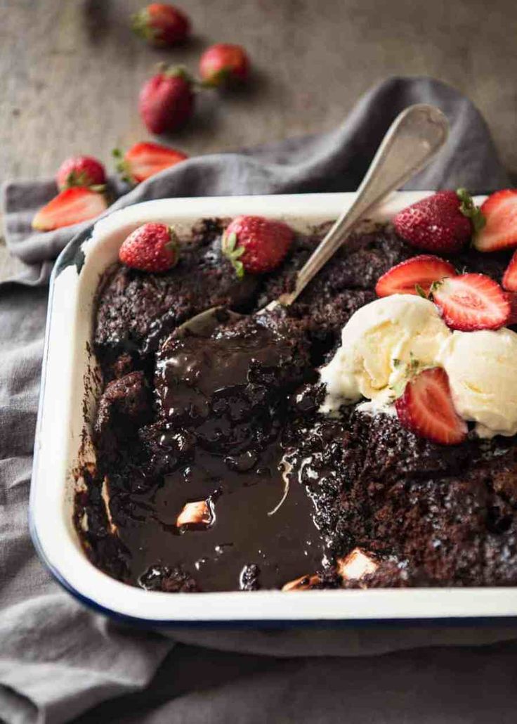 a chocolate cake with ice cream and strawberries on top is in a white dish