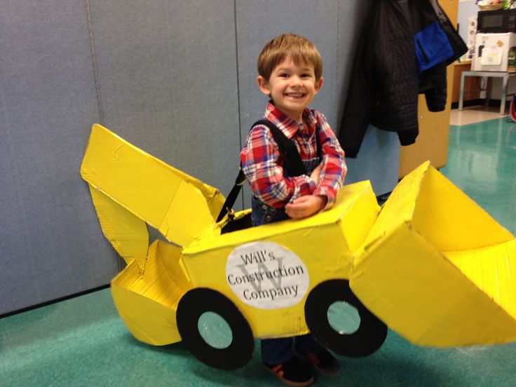 a young boy standing in front of a yellow construction vehicle costume made out of cardboard