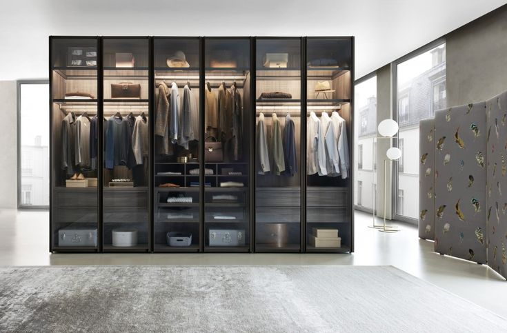 a walk in closet filled with clothes next to a large wall mounted mirror and light fixture