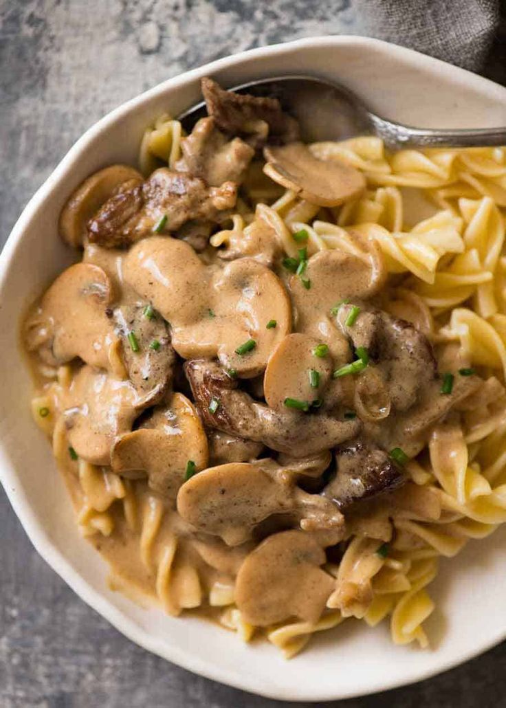 a white bowl filled with pasta covered in mushroom gravy next to a spoon