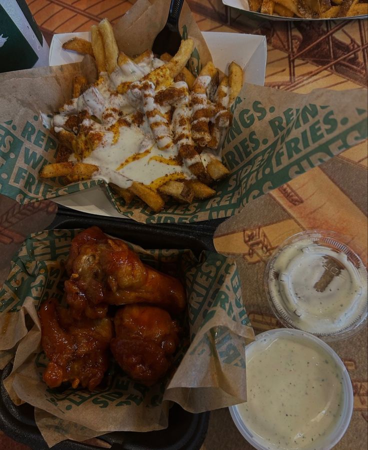 two baskets filled with food sitting on top of a table next to fries and dips