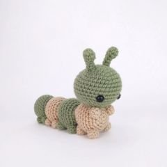 a small crocheted green and beige caterpillar sitting on its side with one eye open