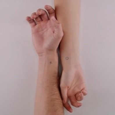 two hands holding each other with tattoos on their arm and wrist, both showing the same tattoo