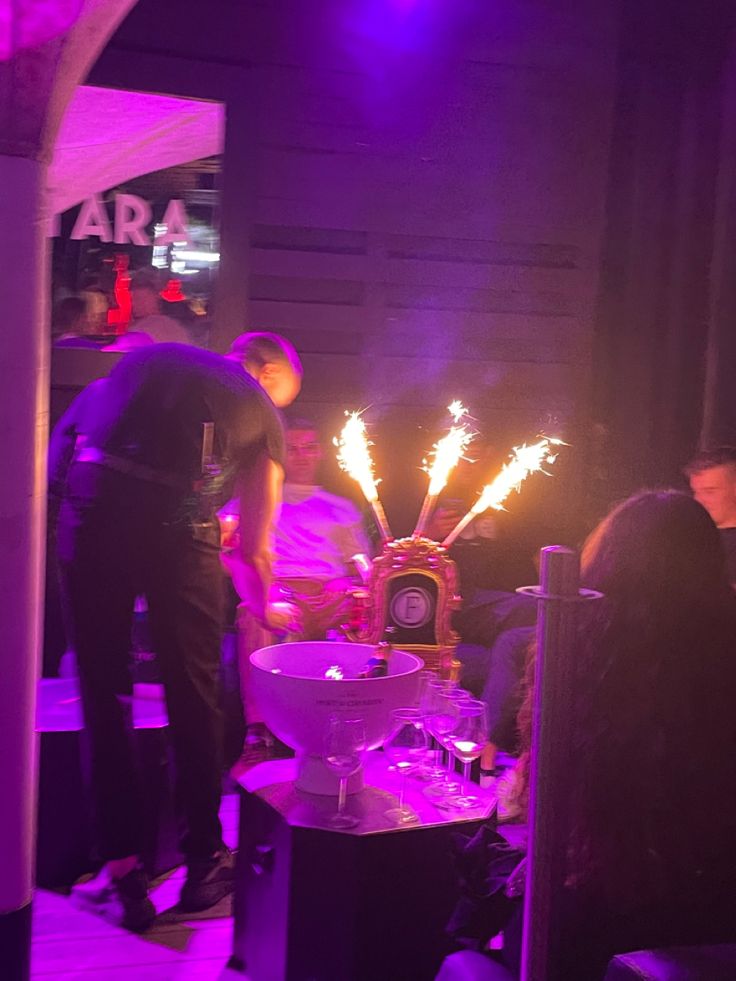 some people are gathered around a cake with candles on it and purple lights in the background