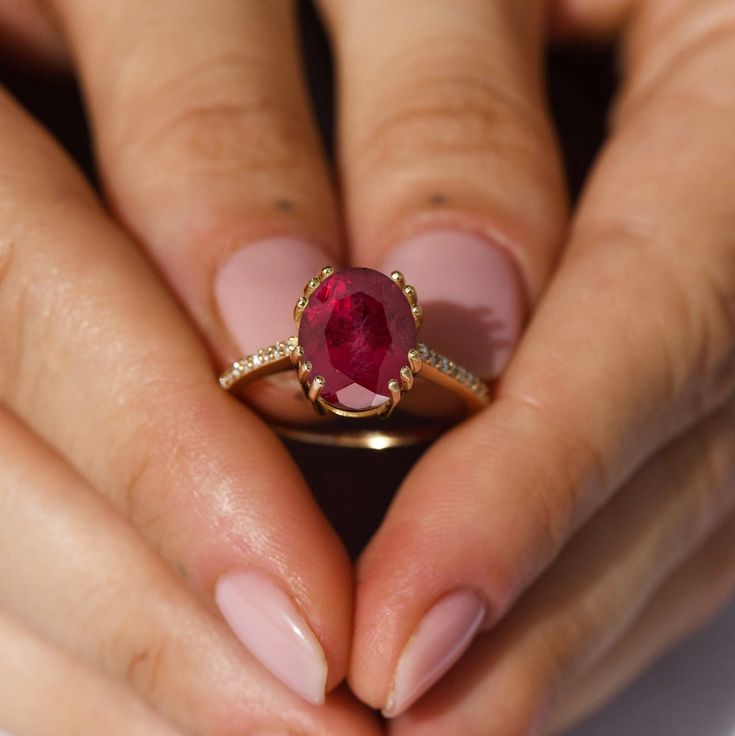 a woman's hands holding a ring with a large red stone in the middle