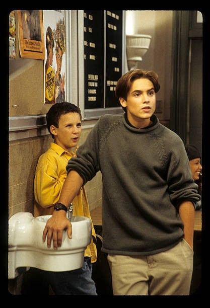 two young men standing next to each other near a urinal