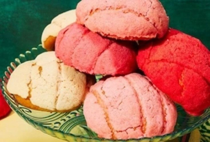 a glass bowl filled with pink and yellow pastries on top of a green table cloth