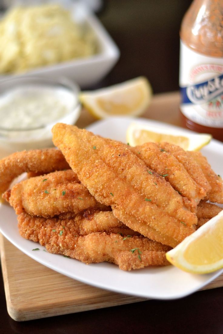 fried fish sticks on a white plate with lemon wedges next to dip and cole slaw