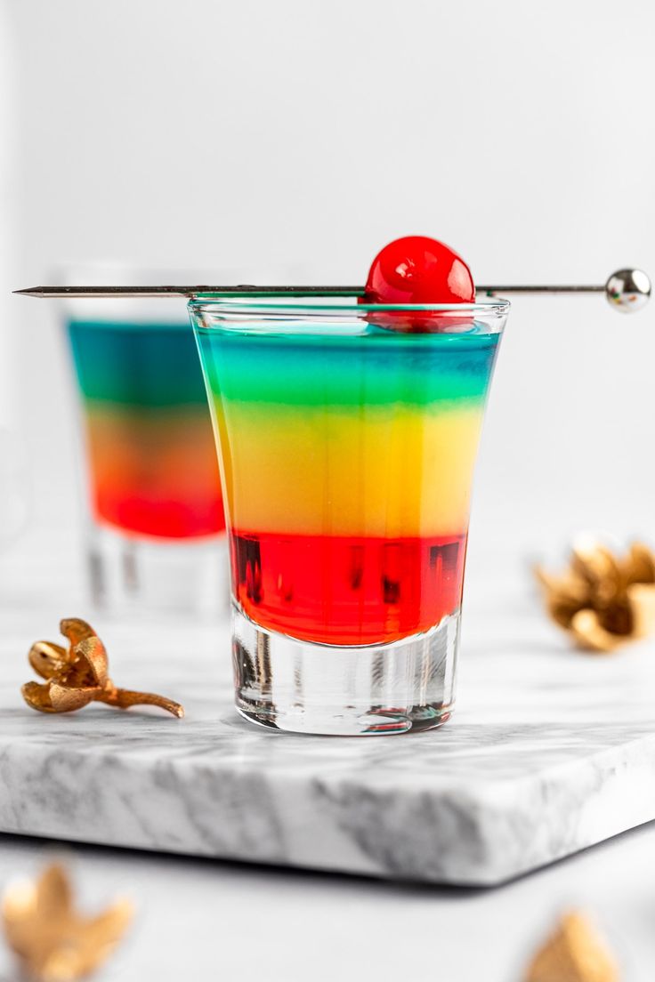 two glasses filled with different colored drinks on top of a marble table next to gold flakes