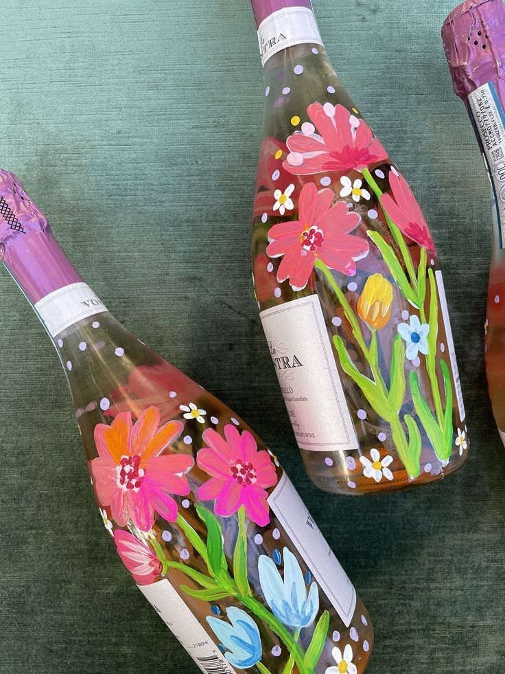 three wine bottles with painted flowers on them sitting on a table next to each other