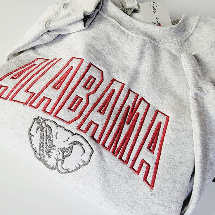 Experience the perfect blend of style and school spirit with our Alabama Elephant Crewneck Sweatshirt or Hoodie! Crafted in a classic ash grey hue, this shirt is designed to keep you cozy and comfortable, whether you're cheering in the stands or just showing off your roll tide pride around town. At the heart of its design is the iconic "Alabama" embroidery, boldly presented across the center chest. The word is intricately stitched in a vibrant crimson, capturing the essence of the University of Gray T-shirt For College In Fall, Casual Gray Sweatshirt For Game Day, Gray Relaxed Fit Collegiate Sweatshirt, Gray Sweatshirt For Game Day In Fall, University Logo Cotton Sweatshirt For Fan Gear, University Logo Cotton Sweatshirt For Fans, University Logo Cotton Sweatshirt Fan Gear, Gray Varsity Top For College, Gray Cotton College Hoodie