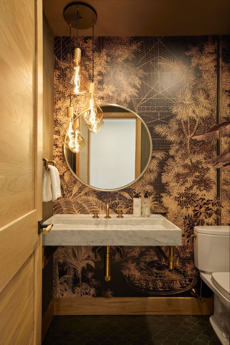 a bathroom with a sink, mirror and toilet in it's corner area next to a wallpapered wall