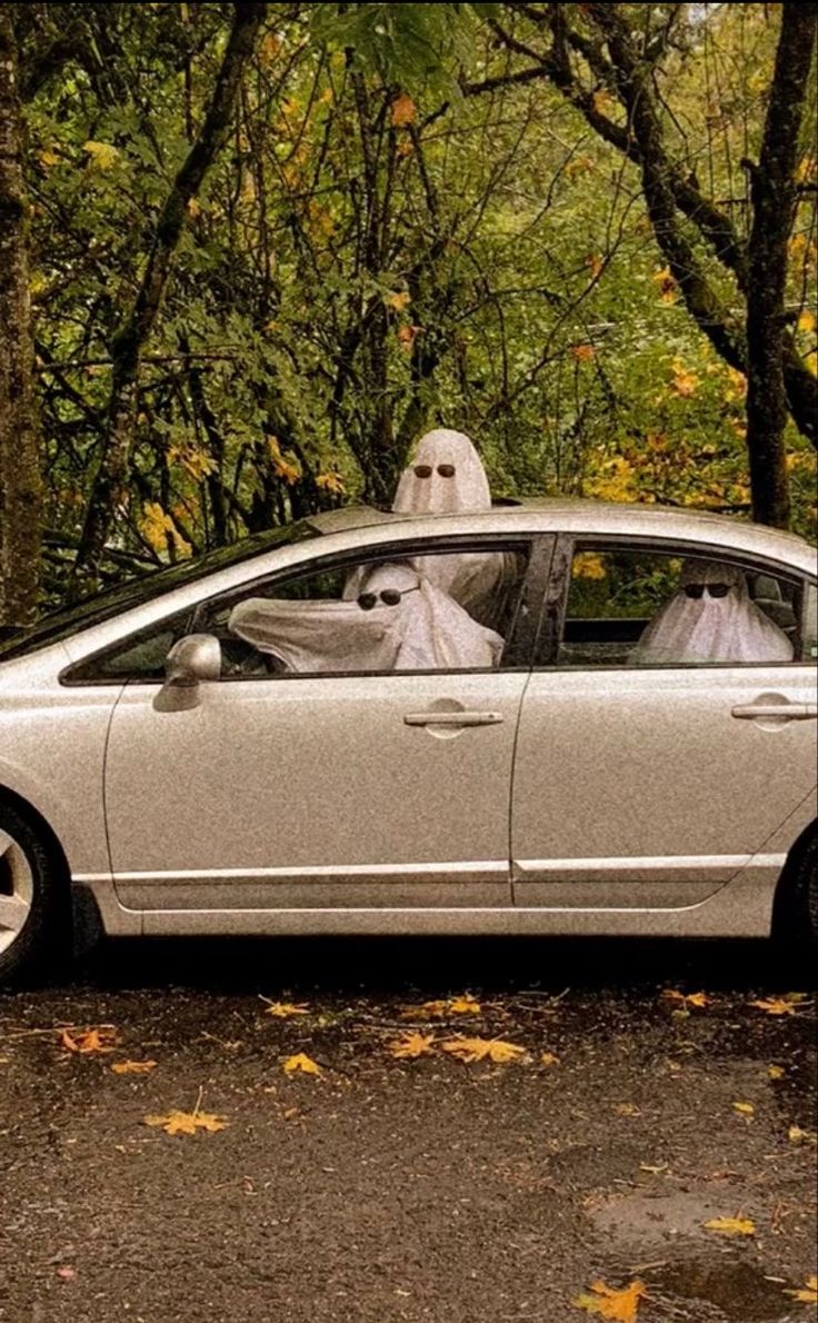 a car with a ghost in the driver's seat driving down a road surrounded by trees